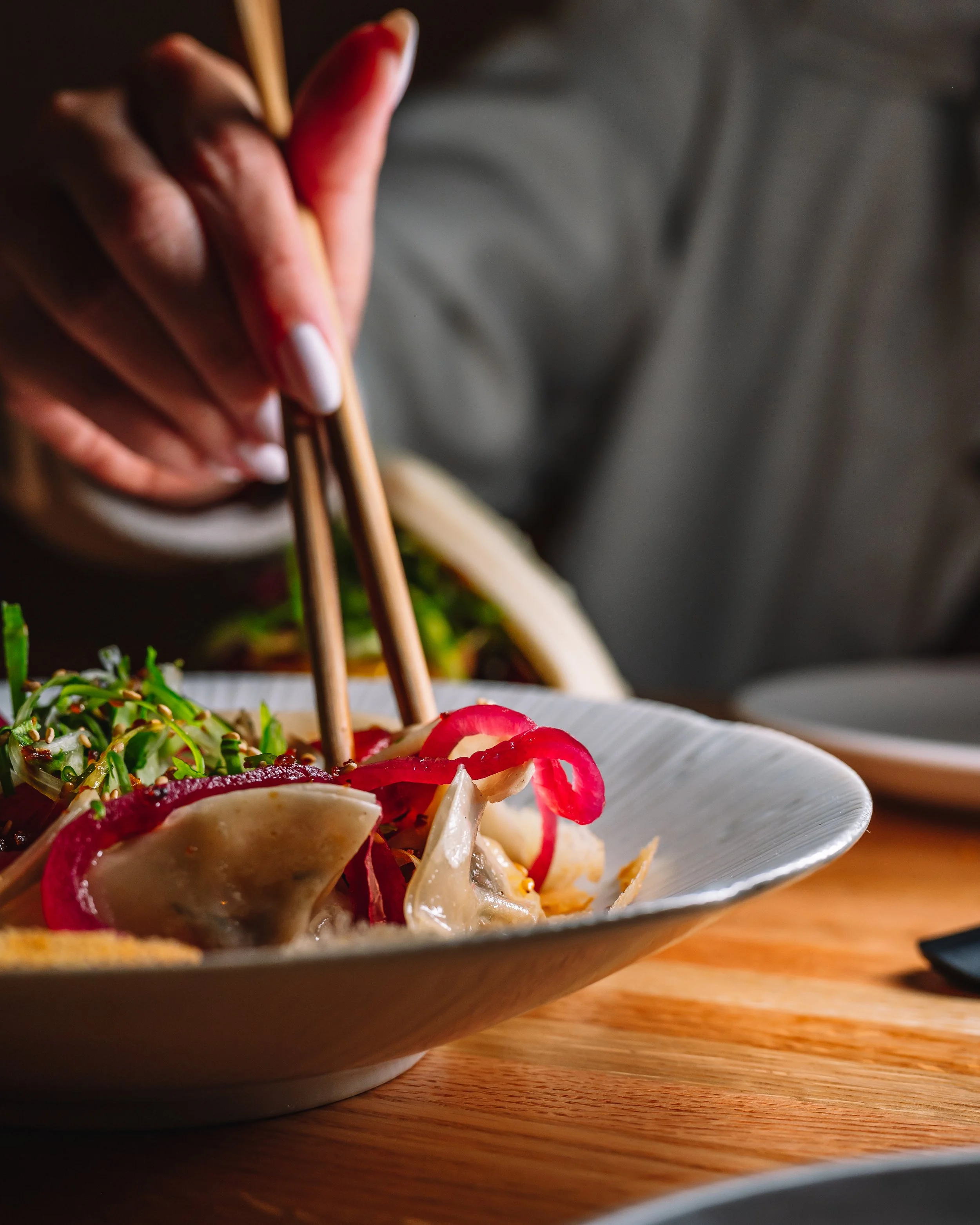 Chicken basil dish being lifted from a bowl with chopsticks