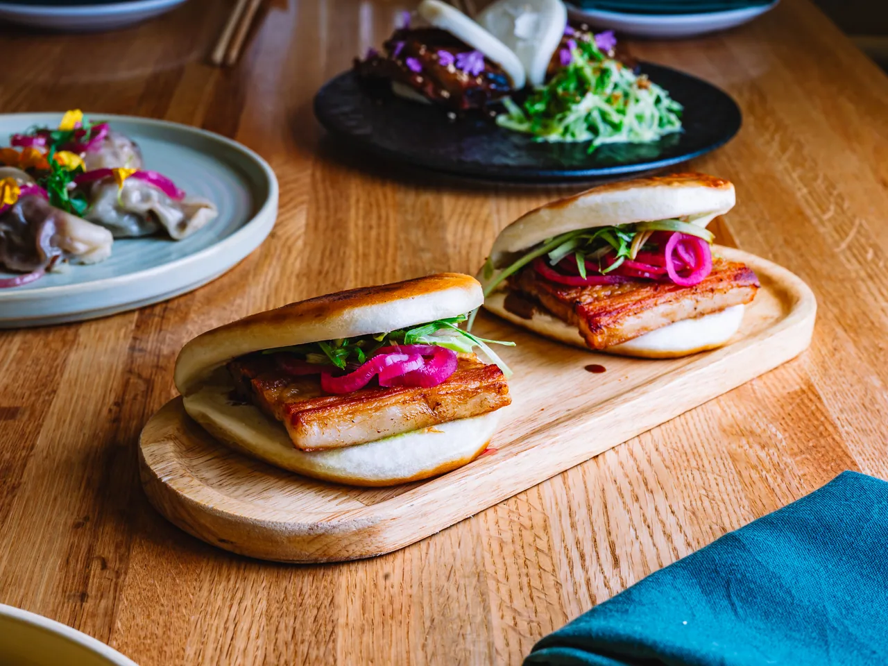 Two filled bao buns on a wooden board among small plates