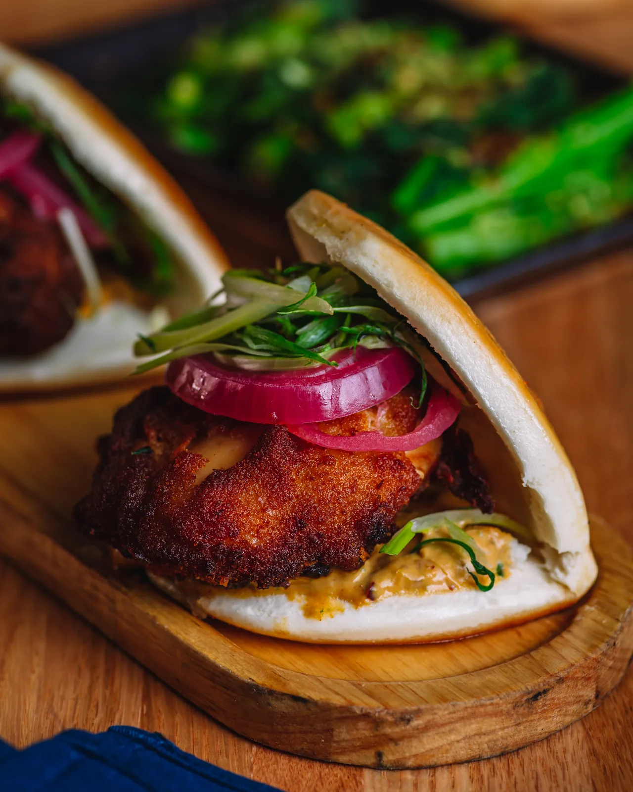 An open bao bun filled with a glazed patty, herbs and pickled onion