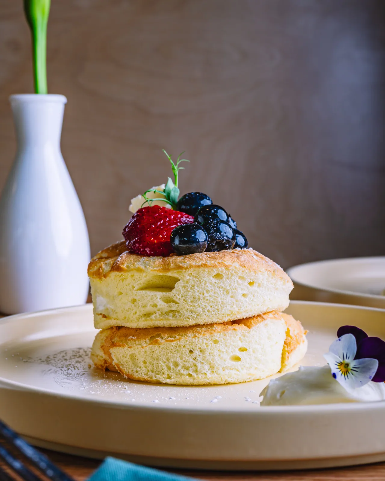 A stack of thick pancakes topped with berries and cream