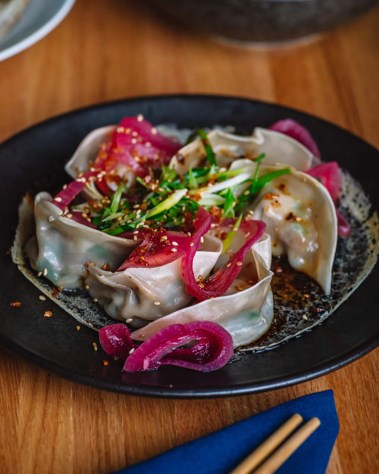 Dumplings with greens and pink pickled onions in a dark bowl
