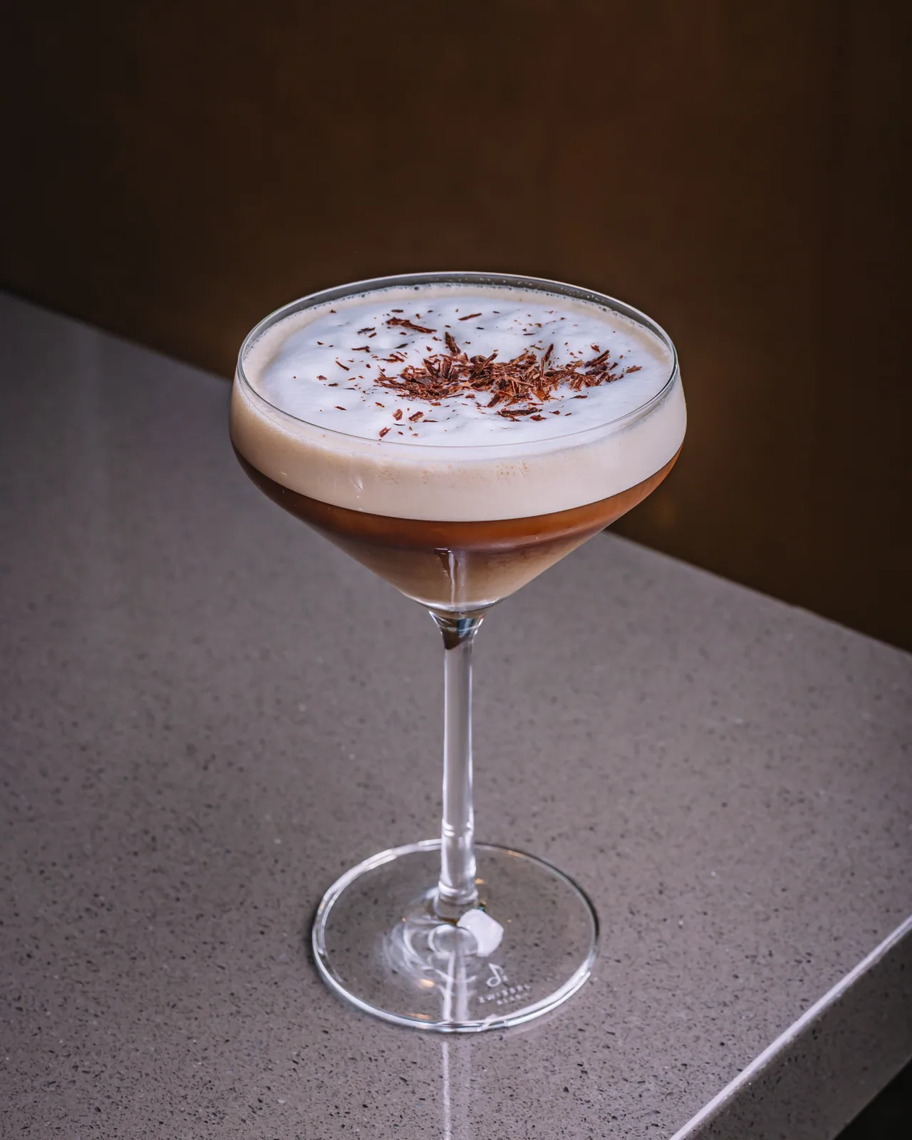A brown drink with pale foam and a dusted garnish in a coupe glass