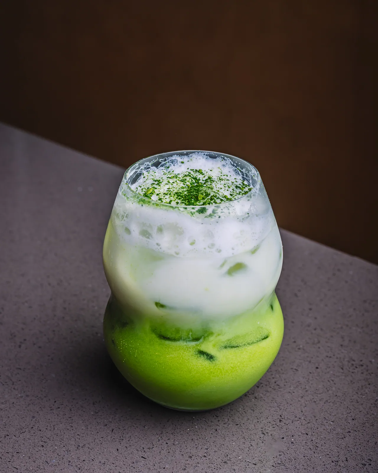 A green iced drink with a pale foamy top in a rounded glass