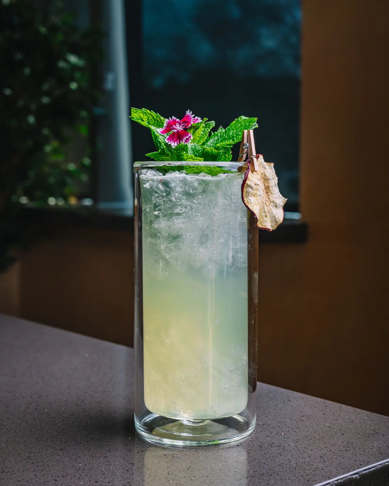 A pale iced drink in a tall glass with mint, flowers and dried fruit
