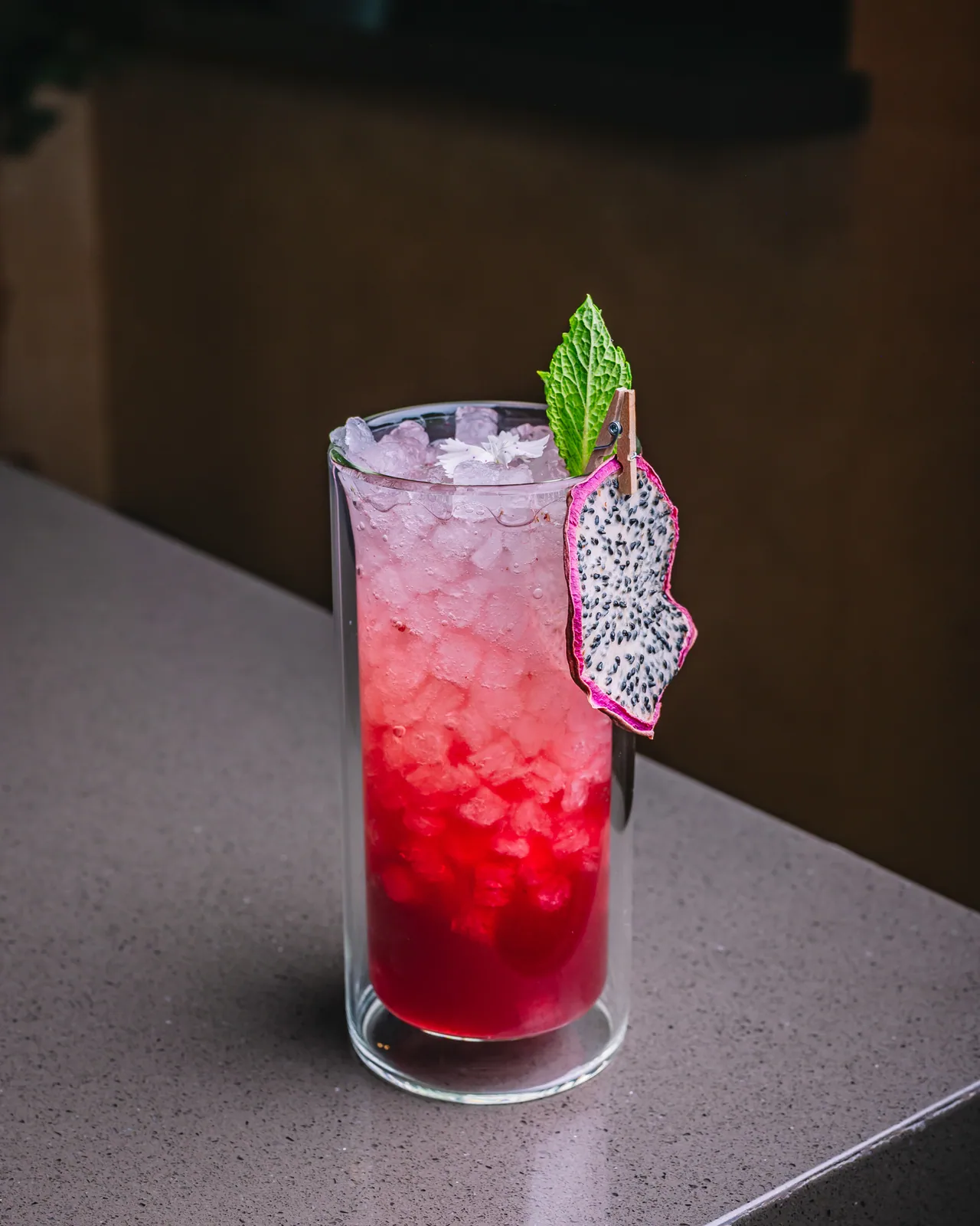 A pink iced drink in a tall glass with mint and dragon fruit garnish
