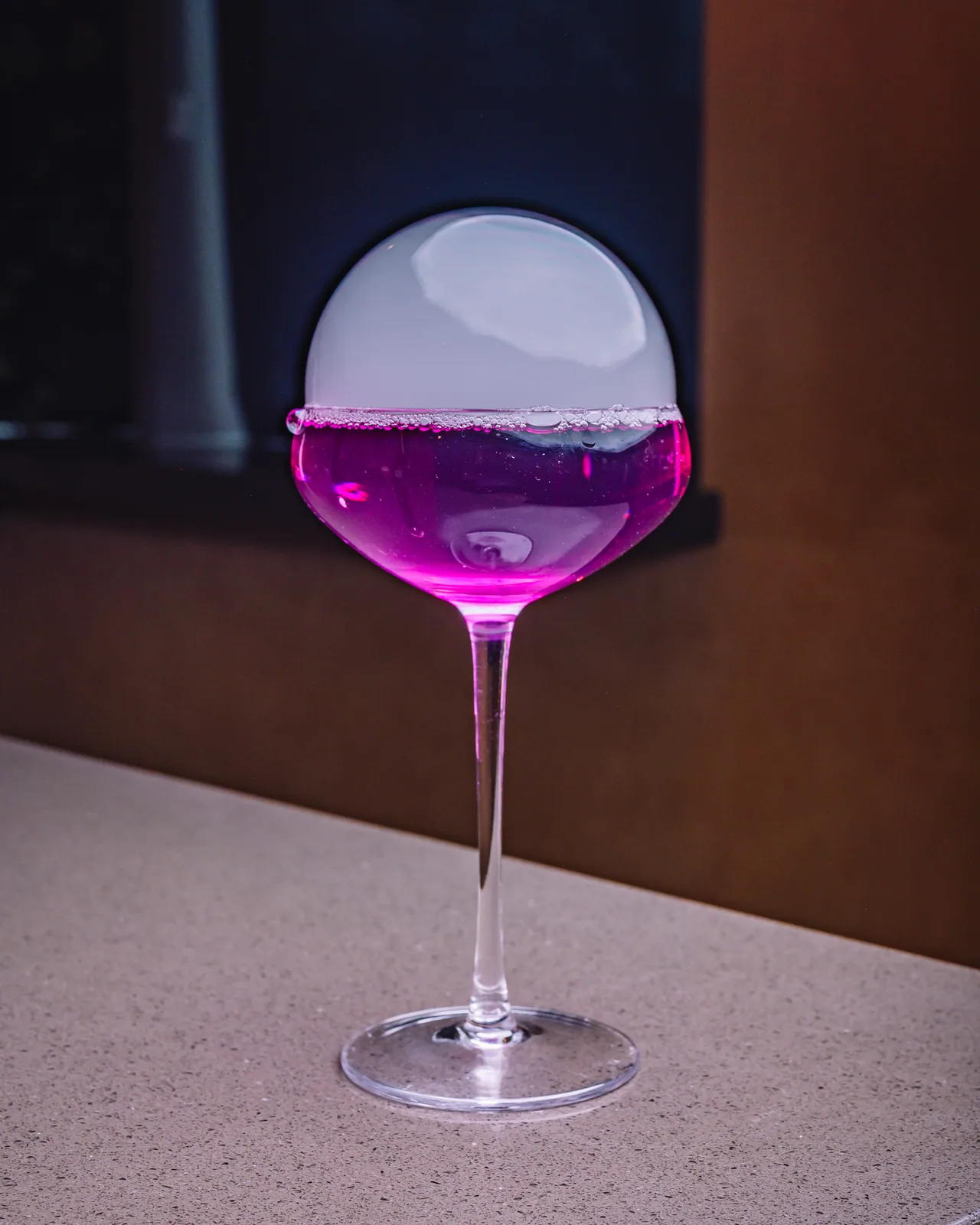 A vivid purple drink in a stemmed glass topped with a round bubble
