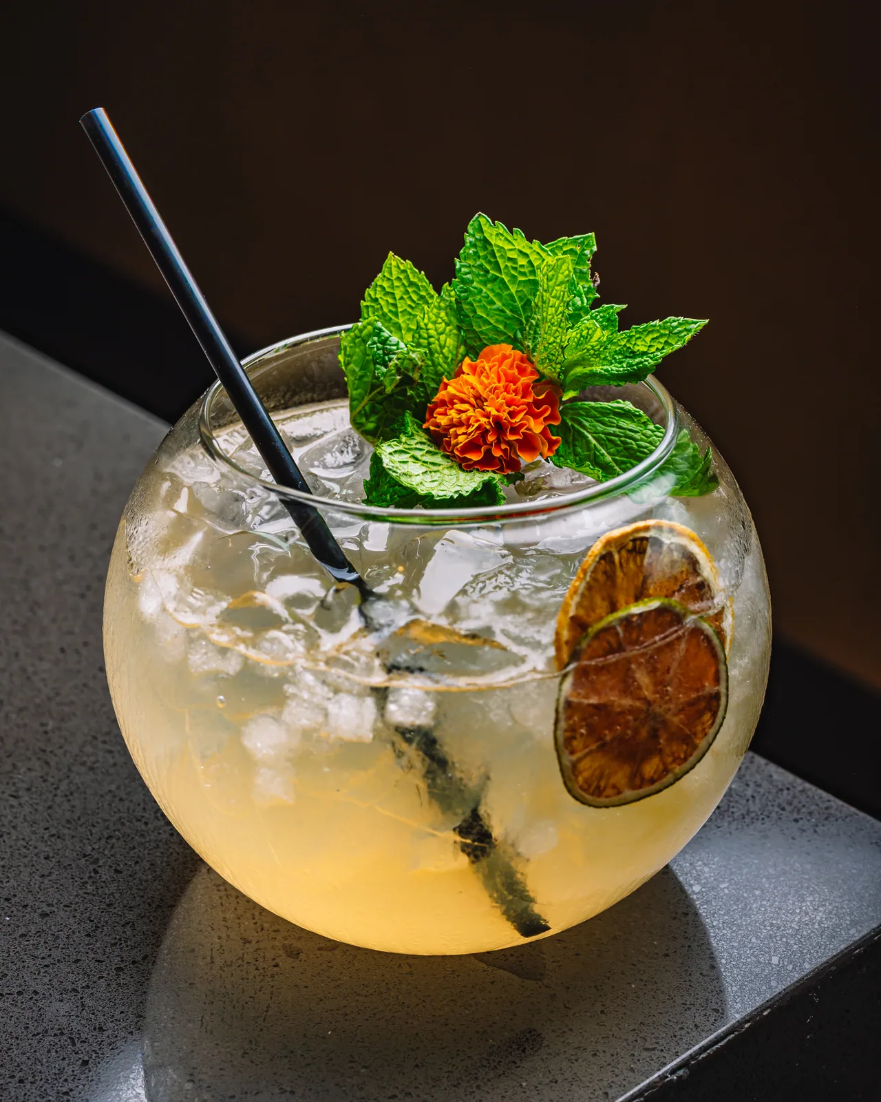 A round bowl-shaped glass filled with ice, citrus and mint