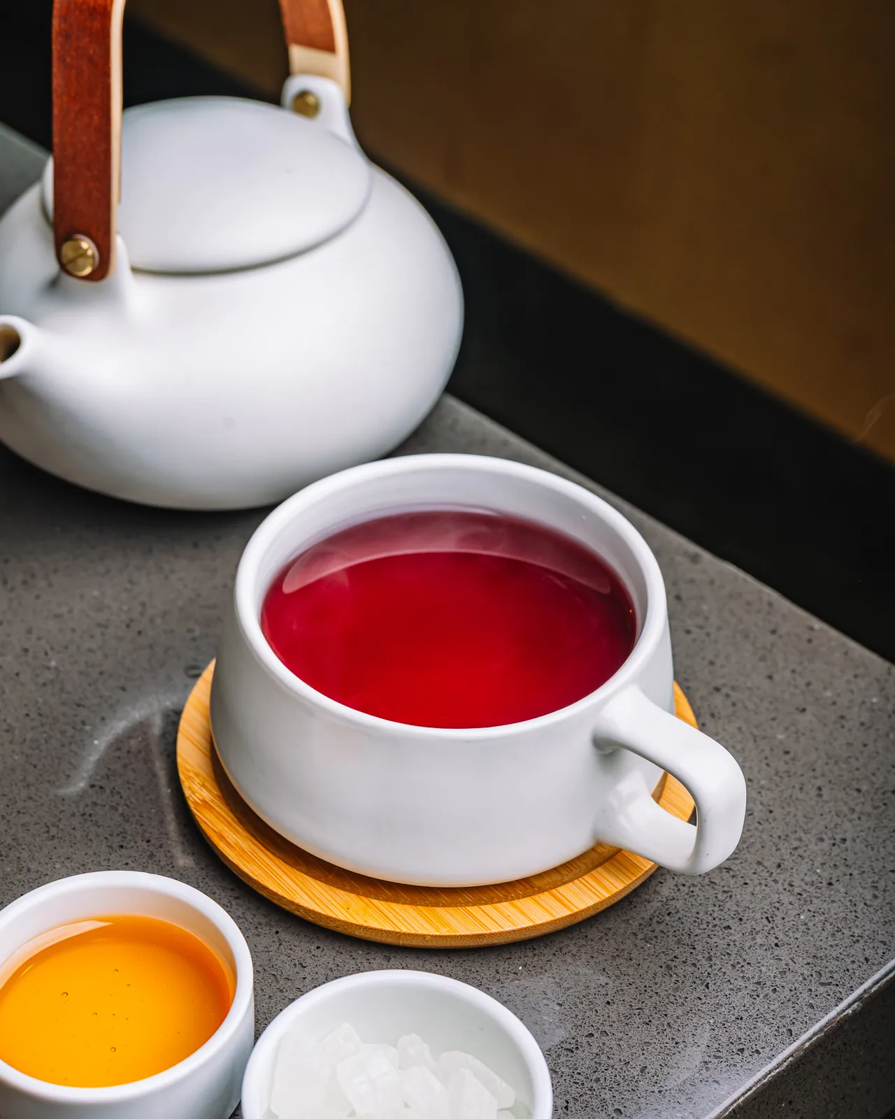 A cup of red tea beside a white teapot and citrus slices