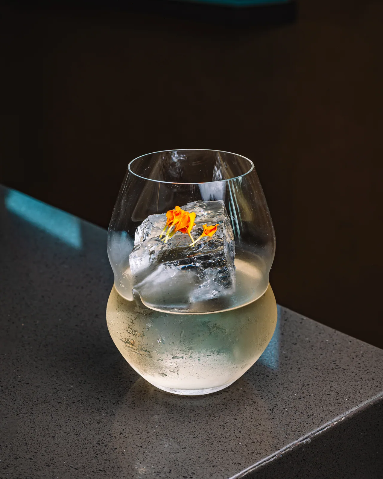 Clear drink over a large ice sphere with a flower garnish