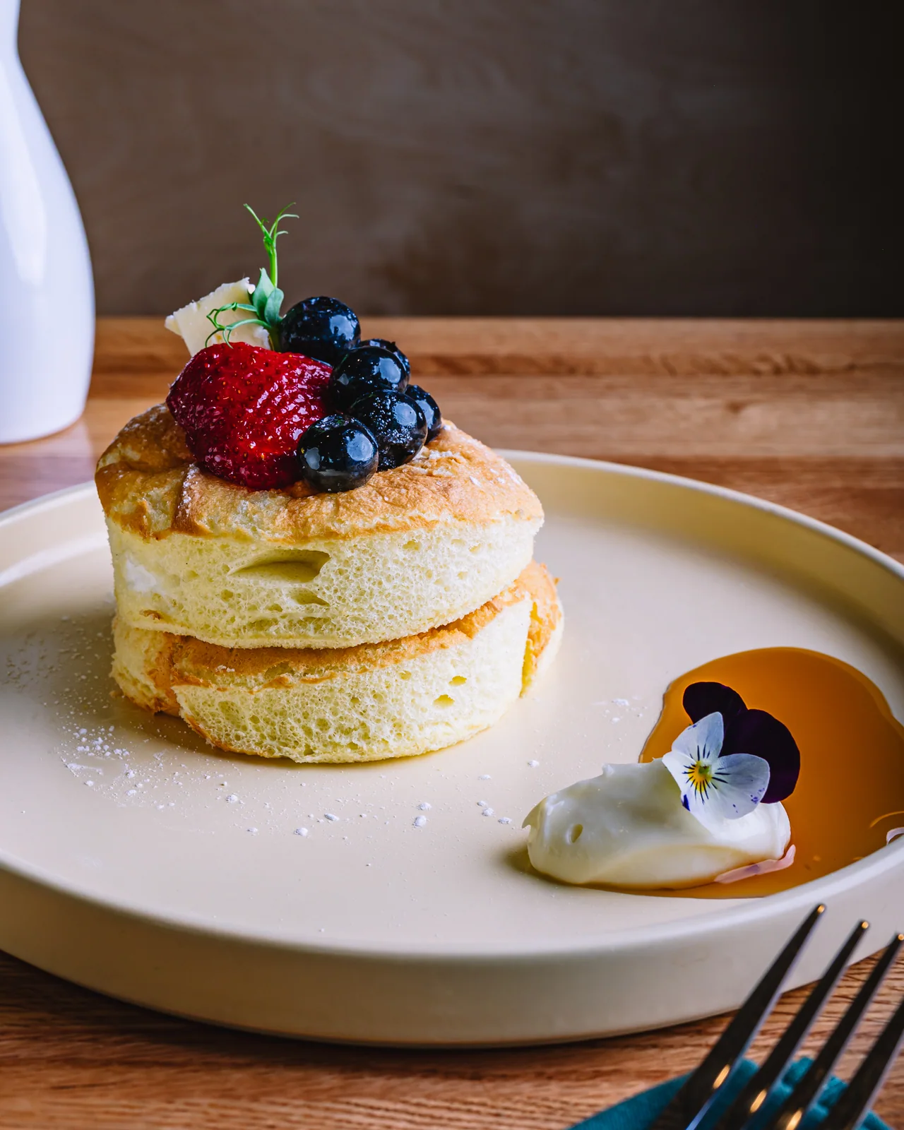 A stack of pancakes topped with berries and cream on a white plate